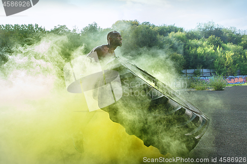 Image of Handsome muscular man flipping big tire outdoor.