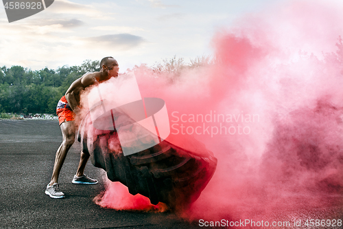 Image of Handsome muscular man flipping big tire outdoor.