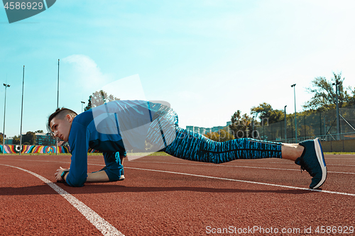 Image of Man runner stretching legs preparing for run training on stadium tracks doing warm-up