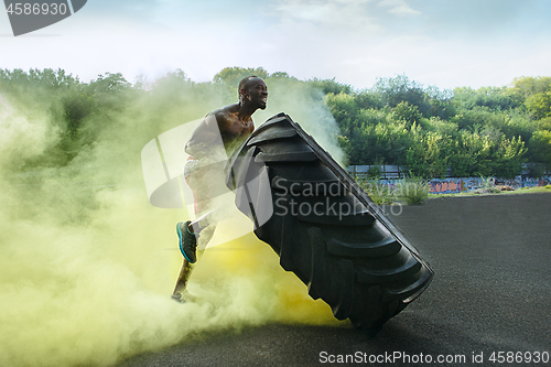 Image of Handsome muscular man flipping big tire outdoor.