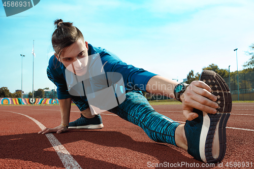 Image of Man runner stretching legs preparing for run training on stadium tracks doing warm-up