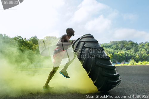 Image of Handsome muscular man flipping big tire outdoor.