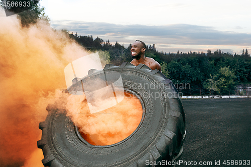 Image of Handsome muscular man flipping big tire outdoor.