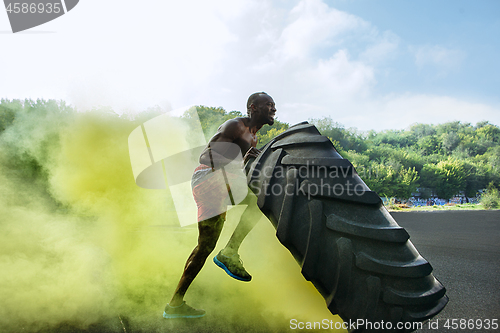 Image of Handsome muscular man flipping big tire outdoor.