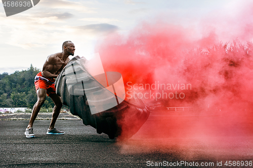 Image of Handsome muscular man flipping big tire outdoor.