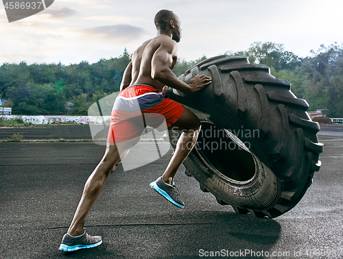 Image of Handsome muscular man flipping big tire outdoor.