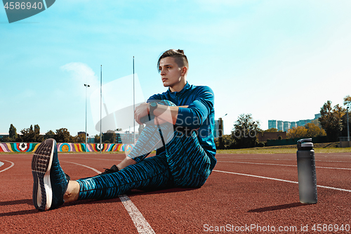 Image of Man runner stretching legs preparing for run training on stadium tracks doing warm-up