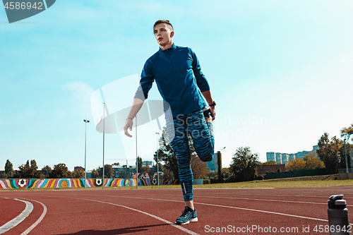 Image of Man runner stretching legs preparing for run training on stadium tracks doing warm-up