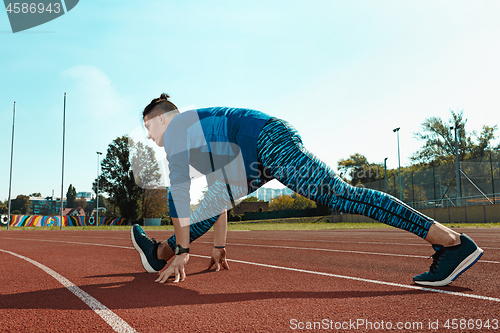 Image of Man runner stretching legs preparing for run training on stadium tracks doing warm-up