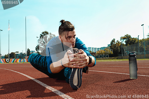 Image of Man runner stretching legs preparing for run training on stadium tracks doing warm-up