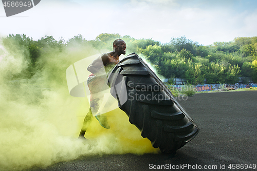 Image of Handsome muscular man flipping big tire outdoor.