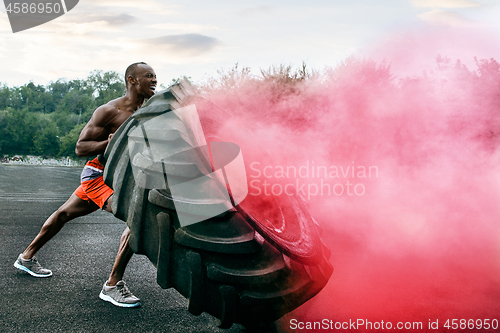 Image of Handsome muscular man flipping big tire outdoor.