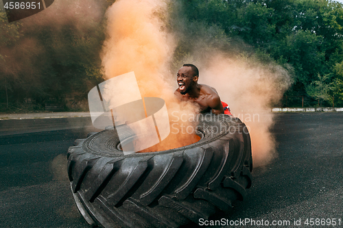 Image of Handsome muscular man flipping big tire outdoor.