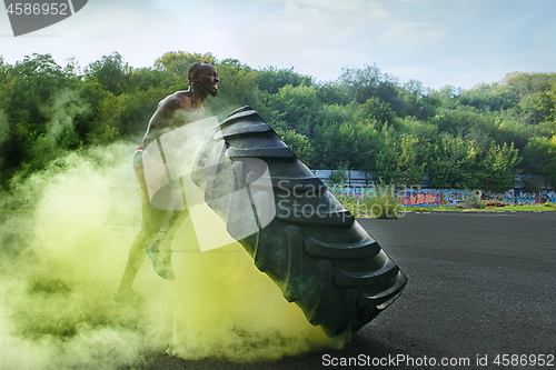 Image of Handsome muscular man flipping big tire outdoor.