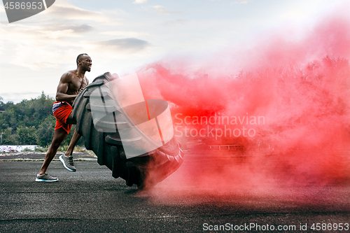 Image of Handsome muscular man flipping big tire outdoor.