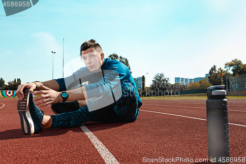 Image of Man runner stretching legs preparing for run training on stadium tracks doing warm-up