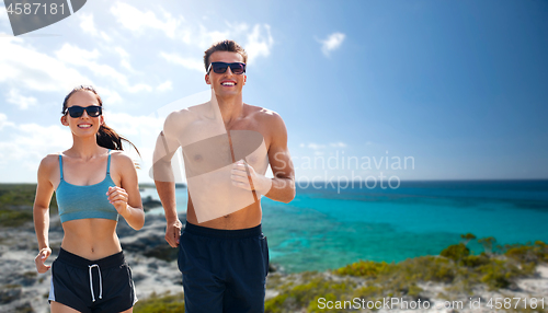 Image of couple in sports clothes running along on beach