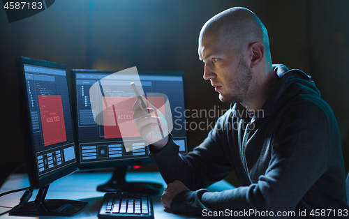 Image of hacker with smartphone and computers in dark room