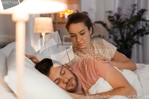 Image of woman wakes her sleeping husband up in bed at home