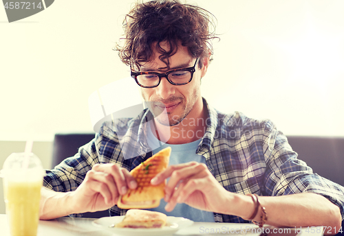 Image of happy man eating sandwich at cafe for lunch