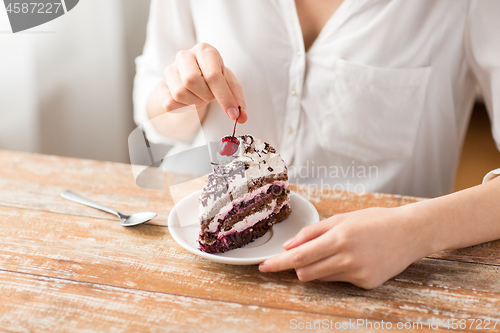 Image of woman taking cherry from piece of chocolate cake