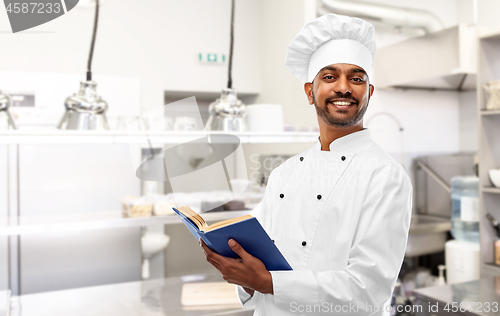 Image of happy indian chef with cookbook at kitchen