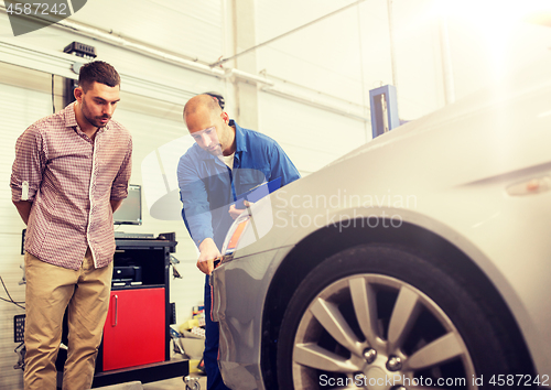 Image of auto mechanic with clipboard and man at car shop