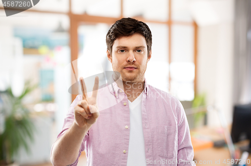 Image of young man showing two fingers over office