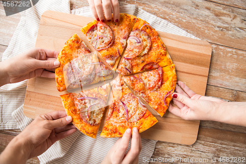 Image of close up of hands sharing pizza on wooden table