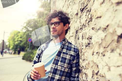 Image of man in eyeglasses drinking coffee over street wall