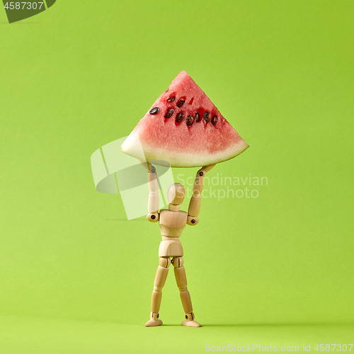 Image of Energy wooden mannequin model holds slice of ripe water melon.
