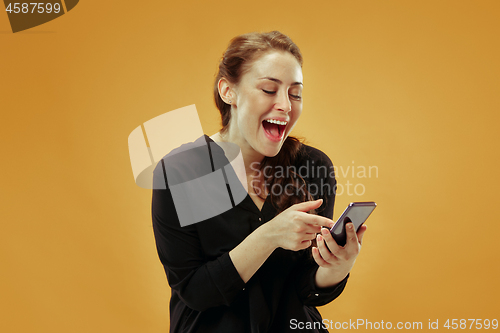 Image of Young beautiful woman using mobile phone studio on gold color background