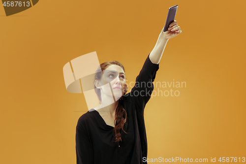 Image of Portrait of a happy smiling casual girl showing blank screen mobile phone isolated over gold background