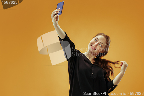 Image of Portrait of a happy smiling casual girl showing blank screen mobile phone isolated over gold background