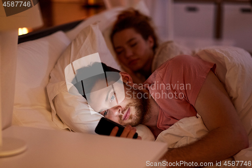 Image of man using smartphone while girlfriend is sleeping