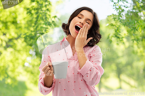 Image of happy yawning young woman in pajama with coffee