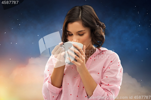 Image of woman in pajama drinking coffee from mug at night