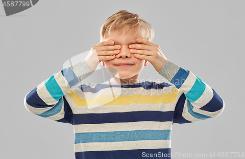 Image of boy in striped pullover closing his eyes by hands