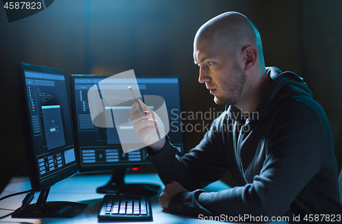 Image of hacker with smartphone and computers in dark room