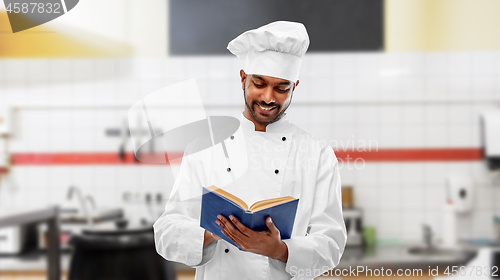 Image of happy indian chef reading cookbook at kitchen