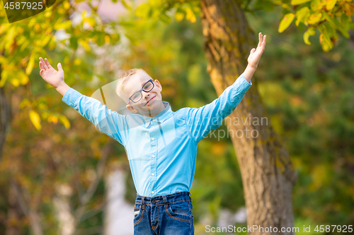 Image of Hilarious seven-year-old boy gleefully raised his hands up in autumn city park