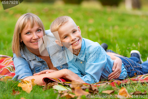 Image of Young mom and teen son lie on bedspread on grass in city park