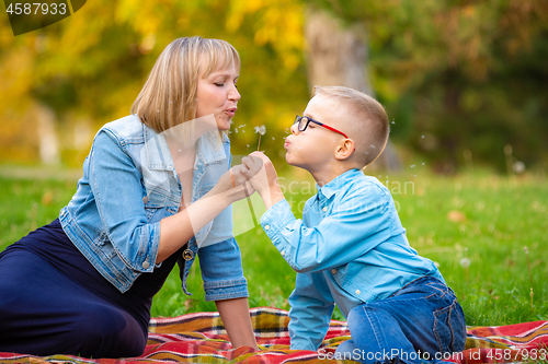 Image of Mom and boy teen sit on green glade and blow off dandelion