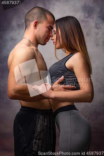 Image of Young loving couple of athletic physique cuddles on grey background