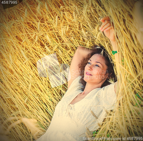 Image of beautiful woman lies among the ears of corn in the field