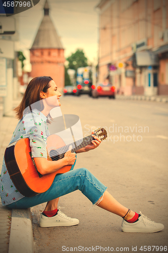 Image of Woman in a blue shirt and jeans with a guitar in the old town