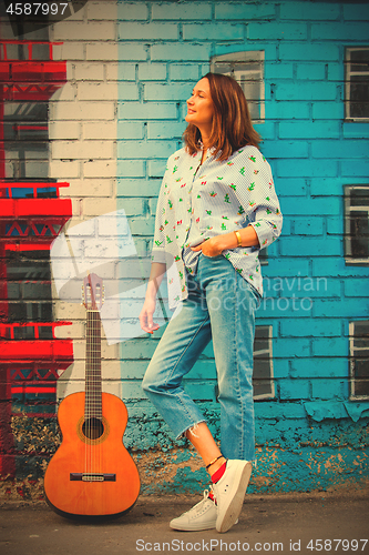 Image of Beautiful brunette woman in blue jeans with a guitar