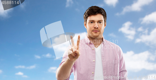 Image of young man showing two fingers over sky