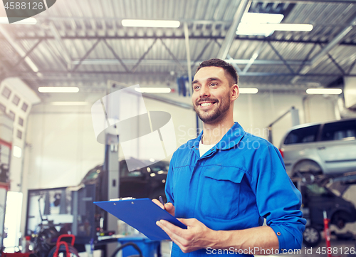 Image of happy mechanic man with clipboard at car workshop