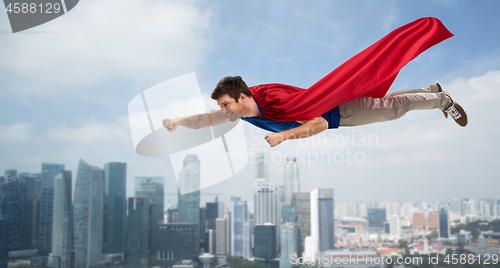 Image of man in red superhero cape flying in air over city